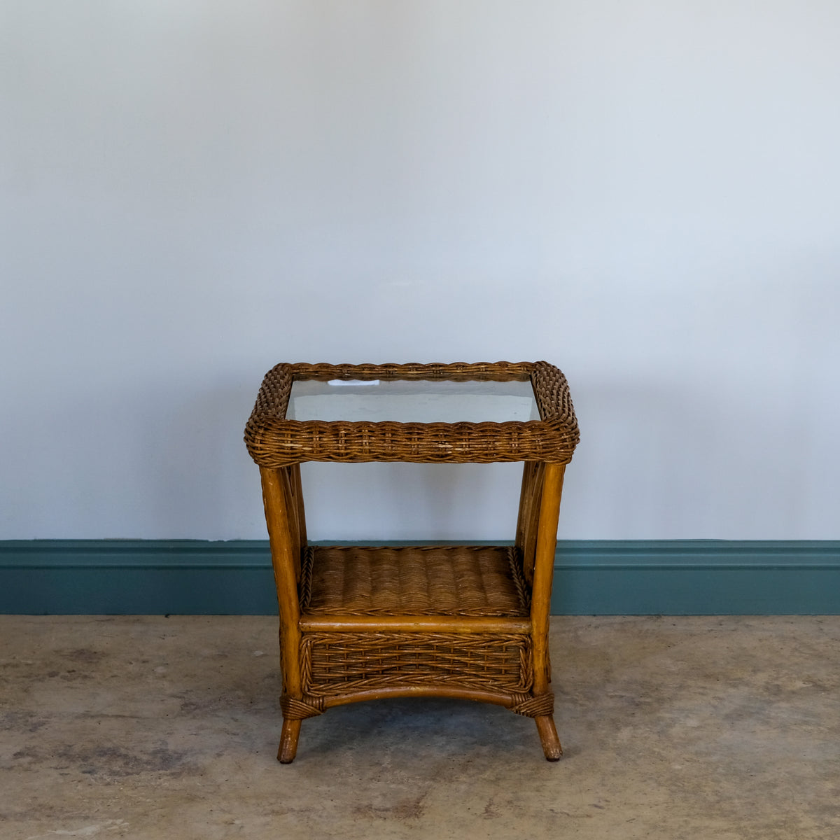 Wicker side table with glass top against a plain wall.
