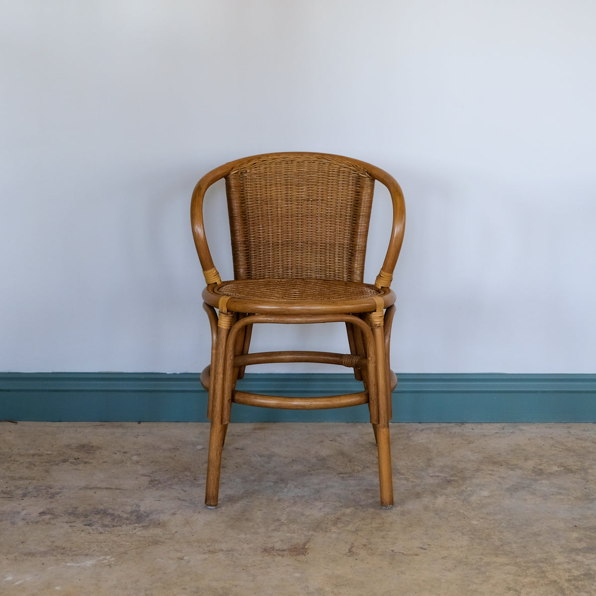Bentwood rattan chair against a plain wall with a blue baseboard.