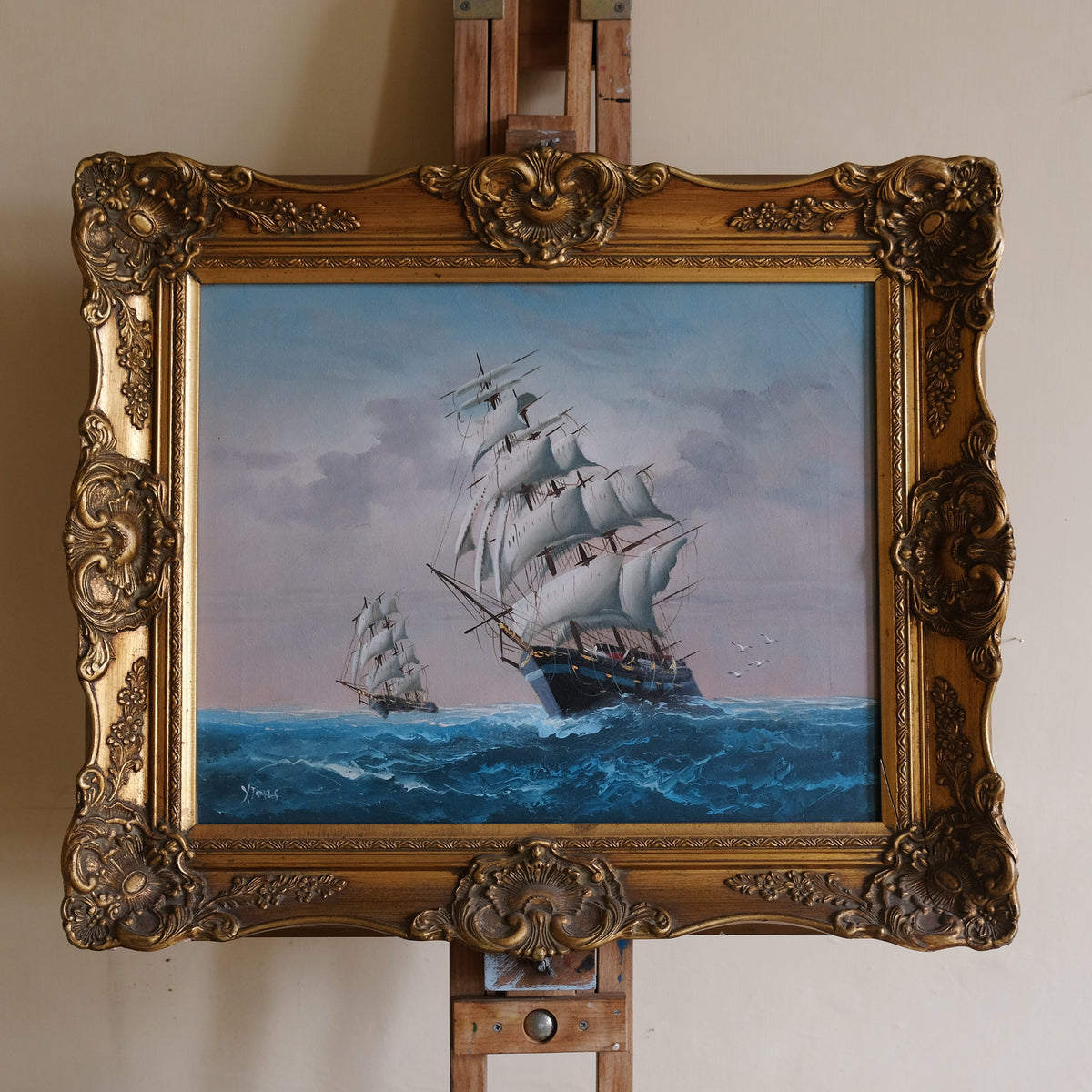 Painting of a ship on an easel with an ornate gold frame.