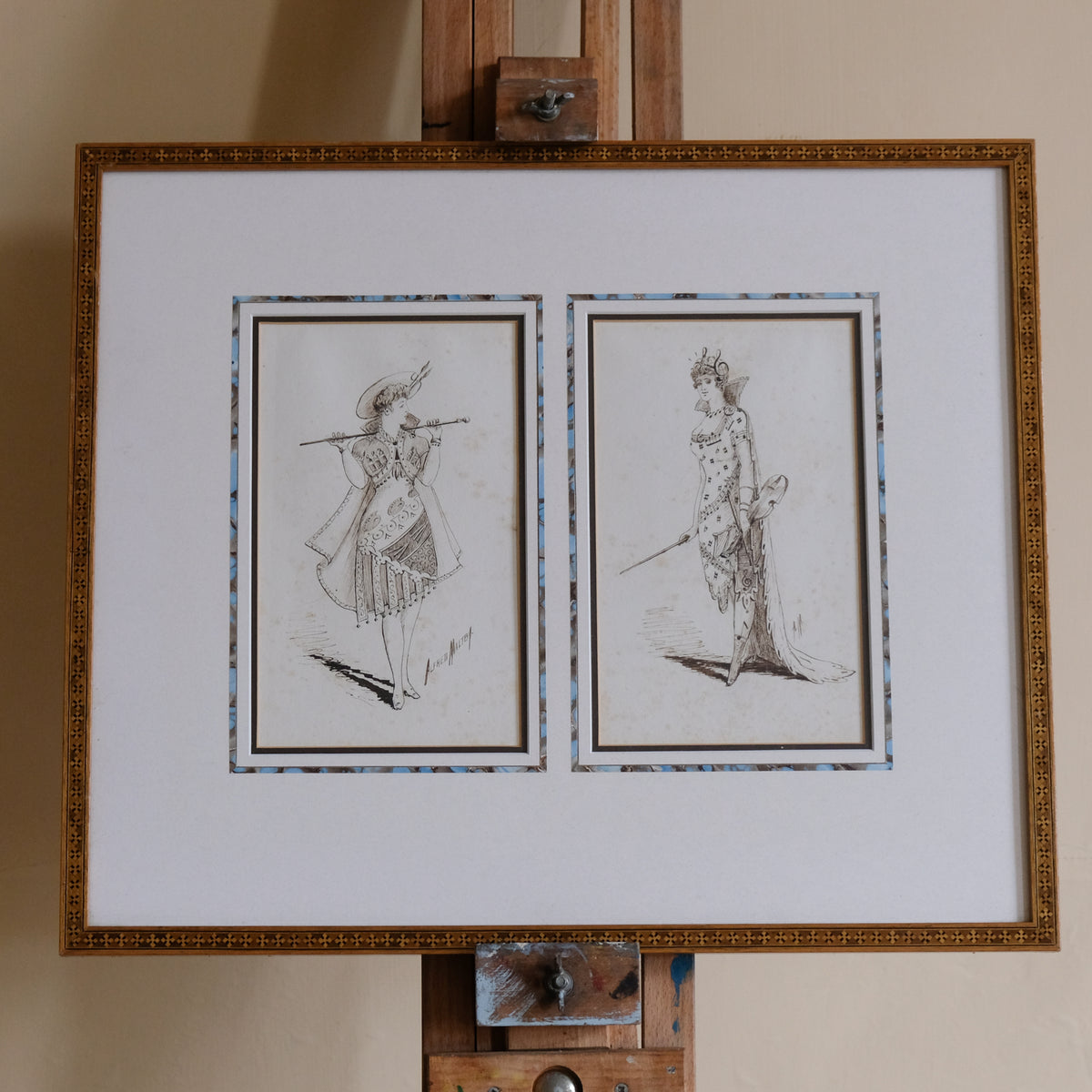 Framed artwork on an easel with two illustrations of women in costume.