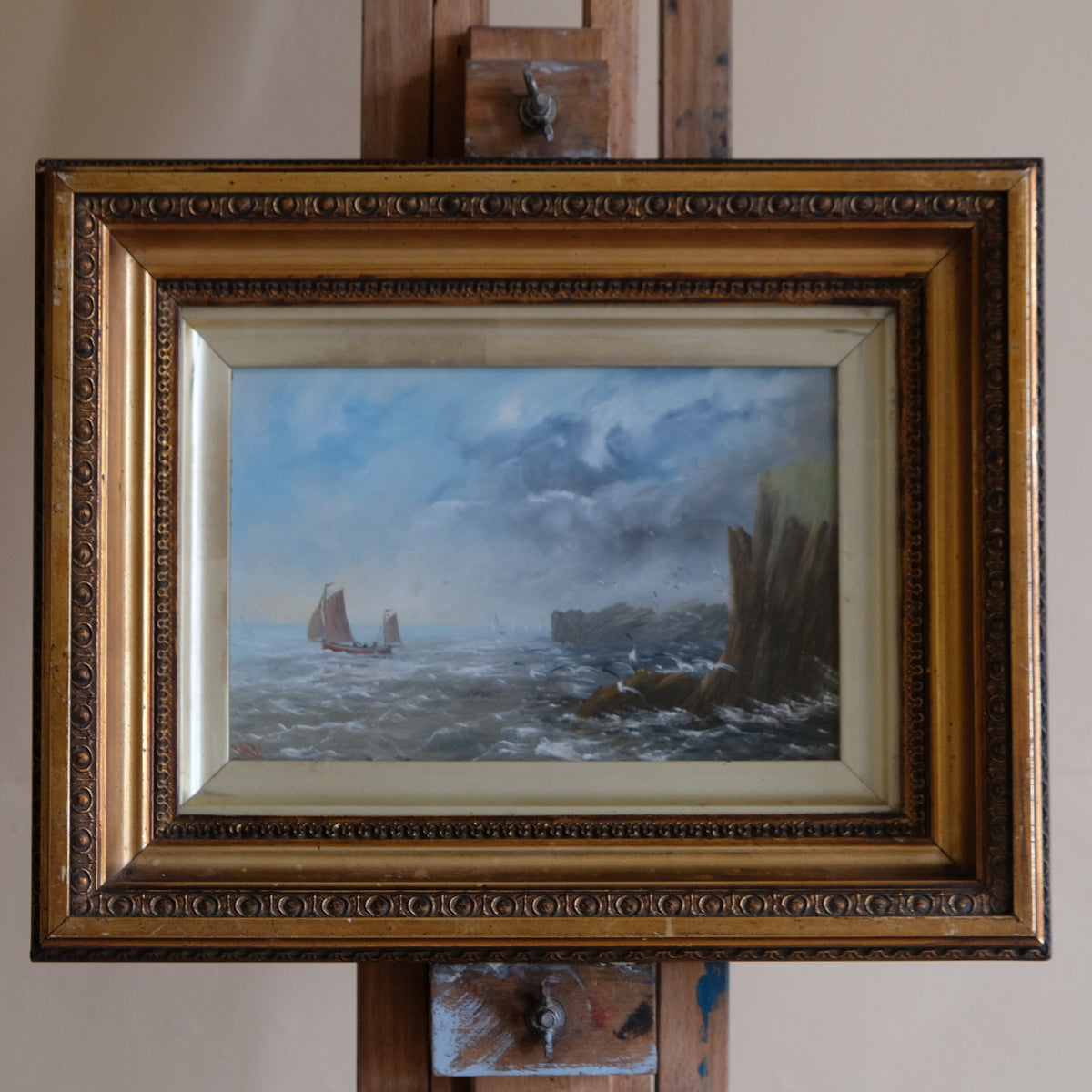 Framed painting of a seascape with a ship and rocky cliffs.